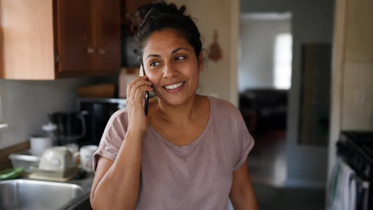A woman smiling while talking on the phone in her kitchen
