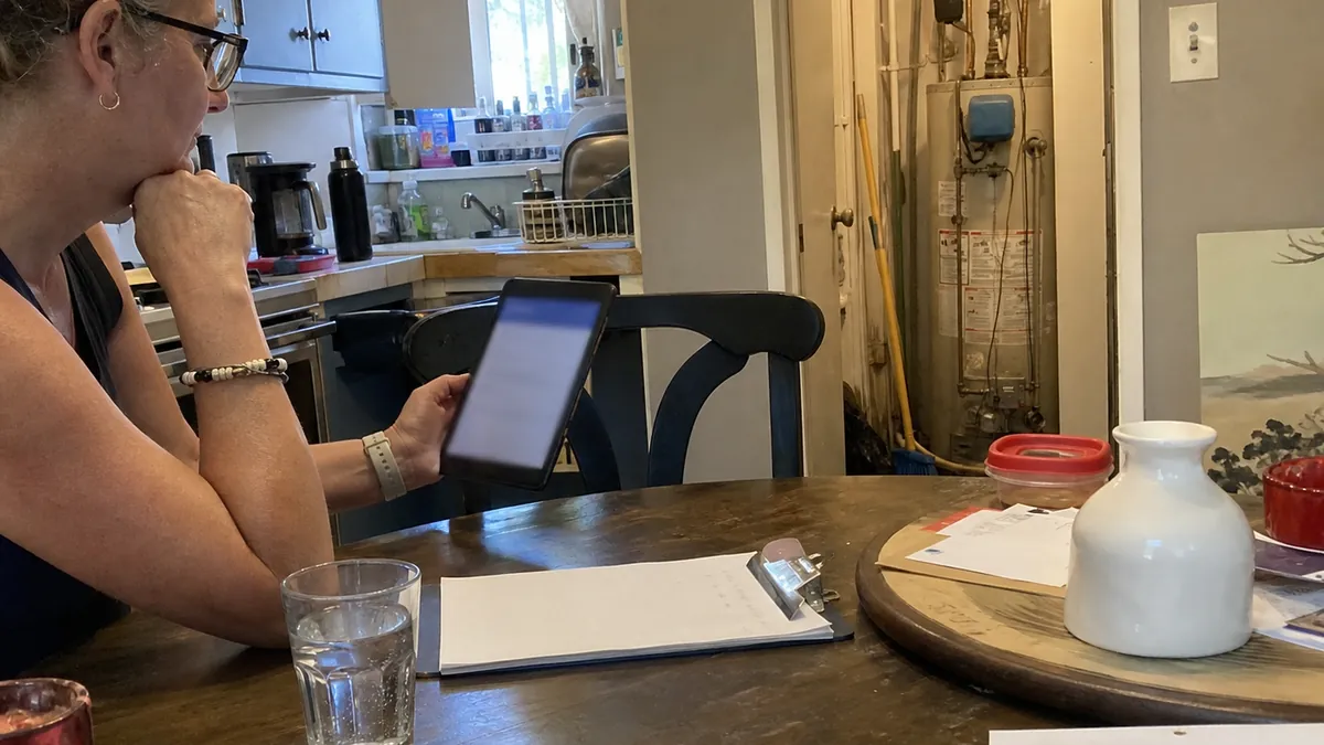 A homeowner at a kitchen table looking at a tablet showing a monthly payment option for a repair
