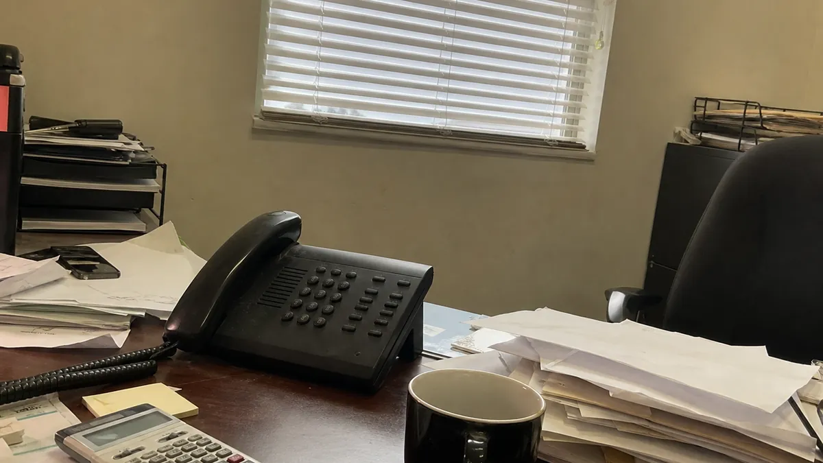 A calculator and payroll paperwork next to a ringing phone on a plumber's desk