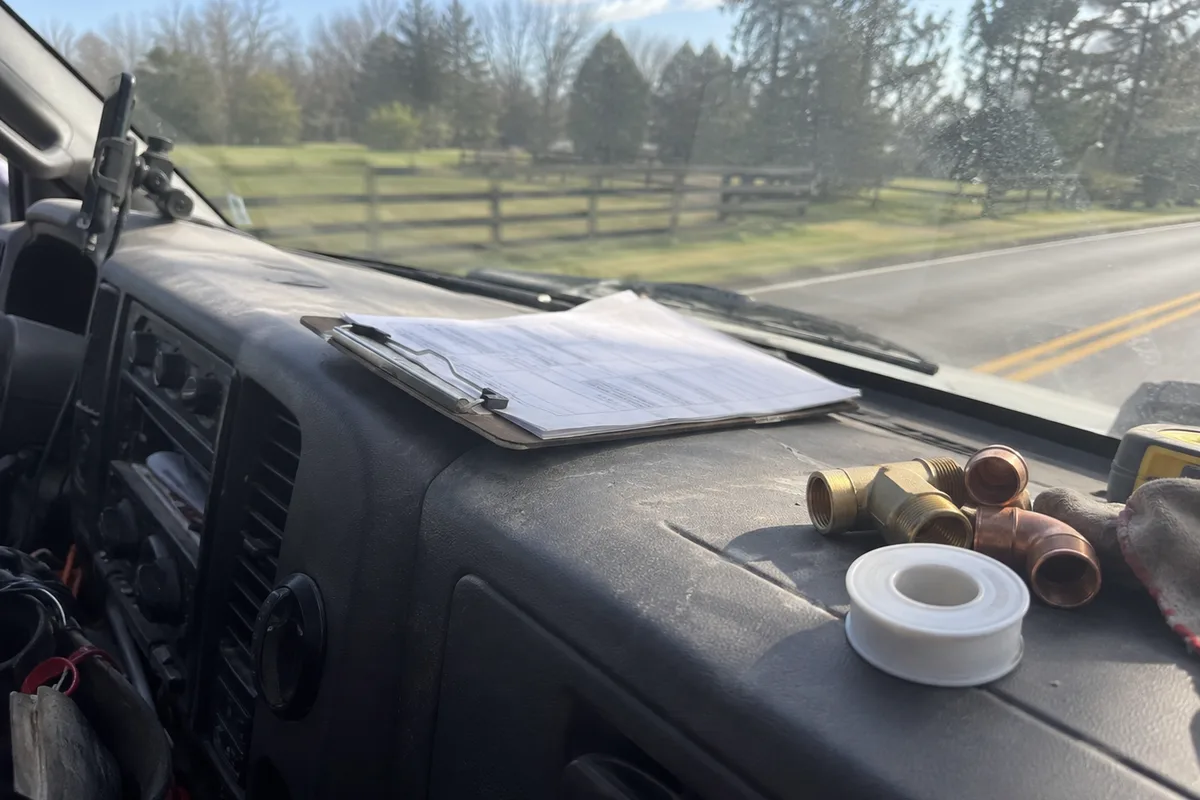 A plumber's work order clipboard on a truck dashboard with a handwritten note