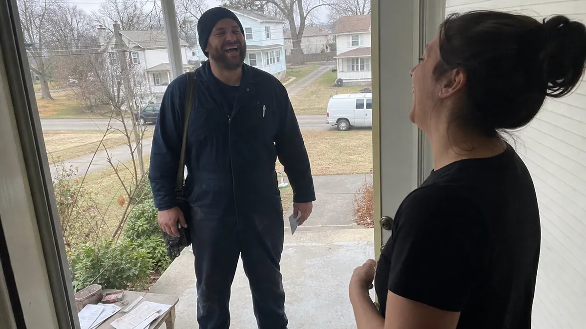A plumber in a navy polo welcomed back at the door by a returning customer