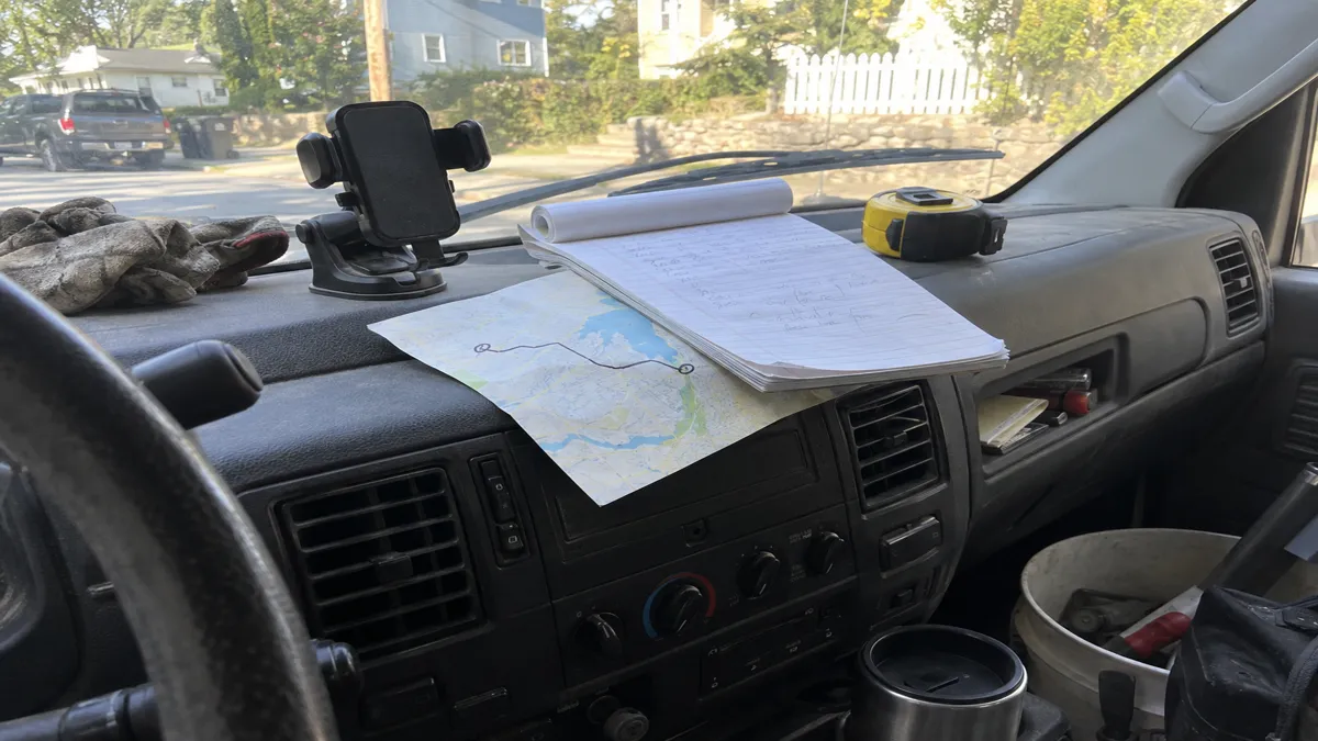 A hand-drawn route sketched on a paper map next to a handwritten intake pad on a work truck's dashboard