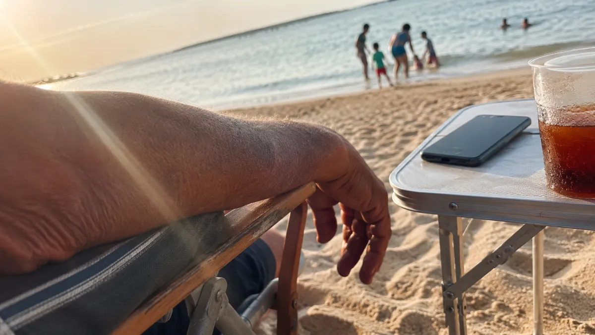 A weathered hand relaxed on a beach chair with a phone face-down on the side table, ignored