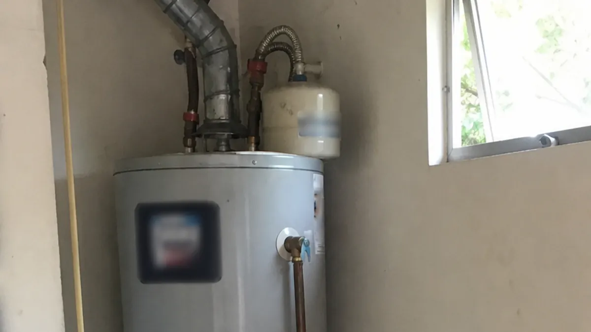 An older residential water heater tank in a garage corner, cold morning light